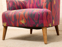 Load image into Gallery viewer, A close-up of a modern armchair upholstered in a bold floral patterned fabric with pink, red, orange, and dark purple tones, featuring tapered wooden legs.
