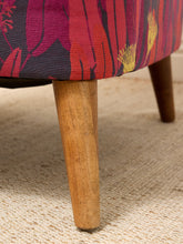 Load image into Gallery viewer, Close-up of a wooden upholstered chair leg on a textured beige rug, showing the patterned fabric in red, pink, and purple tones.
