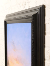 Load image into Gallery viewer, A close-up of a black ornate picture frame leaning against a white painted brick wall, with a pastel sky artwork visible inside the frame.
