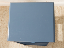 Load image into Gallery viewer, A square, slate blue side table or cabinet with a metal finish, shown from a top-down angle on a woven jute rug.
