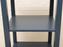 Load image into Gallery viewer, A close-up of a dark slate blue wooden shelving unit with two visible shelves, set against a white painted brick wall.

