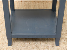 Load image into Gallery viewer, Close-up of a dark blue-gray wooden shelf or side table leg structure resting on a woven beige rug.
