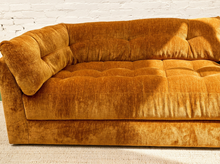 Load image into Gallery viewer, A close-up of a mustard yellow velvet tufted sofa with a matching throw pillow, set against a white brick wall and light-colored carpet.
