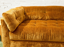 Load image into Gallery viewer, A close-up of a mustard yellow velvet tufted sofa corner against a white brick wall.
