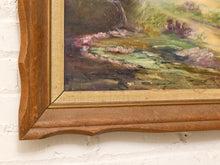 Load image into Gallery viewer, Close-up of a framed landscape painting showing a wooden frame corner with a painted scene of green, brown, and pink water or marshland, mounted on a white brick wall.
