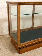 Load image into Gallery viewer, A vintage wooden display case with glass doors and shelves, set against a white brick wall and light-colored carpet.
