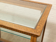 Load image into Gallery viewer, Close-up of a wooden display table with a glass top and decorative carved oak frame, set against a white brick wall background.
