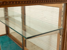 Load image into Gallery viewer, Close-up of a wooden display case or cabinet with clear glass shelves and a decorative carved wood frame, set against a white brick wall background.
