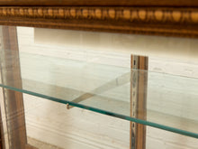 Load image into Gallery viewer, Close-up of a wooden display cabinet or case with a clear glass shelf and metal support brackets, set against a white brick wall.
