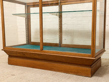 Load image into Gallery viewer, A vintage wooden display case with glass panels and a teal felt-lined base, photographed against a white brick wall and beige carpet.
