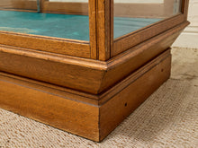 Load image into Gallery viewer, Close-up of the corner base of a wooden display case or cabinet with a glass front panel and turquoise interior lining, resting on a beige woven rug.
