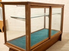 Load image into Gallery viewer, A vintage wooden display case with glass doors and shelves, featuring a teal felt lining, photographed in an indoor room with a white brick wall background.
