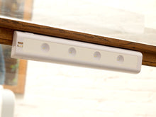 Load image into Gallery viewer, A white linear LED light bar with four circular light elements, mounted underneath a wooden table edge.
