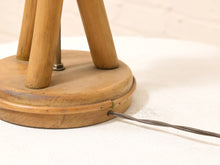 Load image into Gallery viewer, Close-up of a vintage wooden tripod stand with a round base, showing the wood grain and a thin wire attached to the side, resting on a white textured fabric surface.
