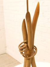Load image into Gallery viewer, A close-up of a decorative lampshade made from several natural bamboo poles bundled together with a coiled rattan or wicker wrap, set against a white brick wall background.
