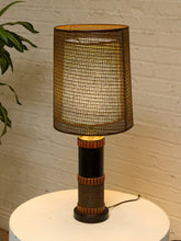Load image into Gallery viewer, Vintage table lamp with tall brown woven shade, black cylindrical base, warm wood accents, and wrapped textured detailing
