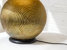 Load image into Gallery viewer, A round table lamp with a textured, ribbed golden-brown glass shade and a black circular base, shown against a white brick wall background.
