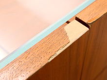 Load image into Gallery viewer, Close-up of a wooden furniture corner showing a worn, chipped section of the wood trim next to a light blue glass edge.

