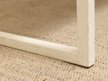 Load image into Gallery viewer, Close-up of a distressed white wooden table leg corner resting on a textured beige woven rug.
