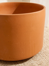 Load image into Gallery viewer, A close-up of a terracotta-colored ceramic planter pot resting on a textured beige woven mat.
