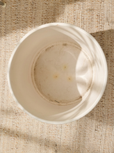 Load image into Gallery viewer, A top-down view of a white ceramic bowl with a rustic, stained interior, placed on a textured beige woven fabric background with soft leaf shadows.
