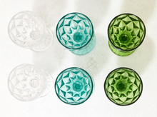 Load image into Gallery viewer, Four vintage-style cut-glass tumblers arranged in a 2x2 grid on a textured white fabric background. The set includes two clear tumblers and two translucent colored tumblers in aqua/teal and light green, each with a faceted geometric starburst pattern.
