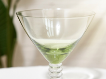 Load image into Gallery viewer, A clear glass martini-style coupe glass with a twisted stem, shown empty on a white surface with a softly blurred indoor background.
