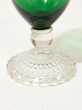 Load image into Gallery viewer, A close-up of a green glass goblet or tumbler with a clear textured glass base, resting on a white textured fabric surface.
