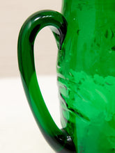 Load image into Gallery viewer, Close-up of a translucent green glass pitcher with a curved handle and textured body, photographed against a light neutral background.

