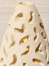 Load image into Gallery viewer, Close-up of a textured beige ceramic decorative vase or candle holder with organic cutout patterns and warm yellow light glowing from within.
