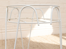 Load image into Gallery viewer, A white metal round side table or plant stand with a minimalist open-frame design, set against a light beige brick wall and textured rug.
