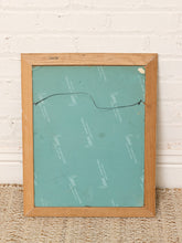 Load image into Gallery viewer, Back of the rectangular wood frame with teal backing and hanging wire, leaning against a white brick wall on a woven rug.
