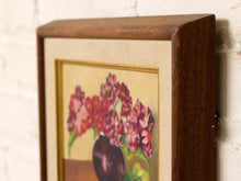 Load image into Gallery viewer, A framed floral art print featuring pink and red flowers in a dark vase against a cream background, housed in a dark brown wooden frame and leaning against a white brick wall.
