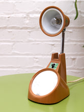 Load image into Gallery viewer, Orange desk lamp upright with its white shade interior, chrome stem, built-in mirror and control switch visible.
