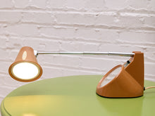 Load image into Gallery viewer, Side view of the orange desk lamp with its chrome stem extended horizontally and illuminated shade directed downward.
