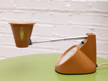 Load image into Gallery viewer, Side view of the orange desk lamp with its chrome stem extended horizontally and shade tilted upward.
