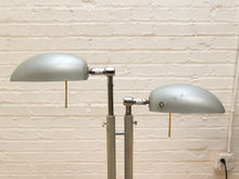 Load image into Gallery viewer, A vintage-style dual-arm floor lamp with matte silver metal shades and adjustable central poles, photographed against a white painted brick wall.
