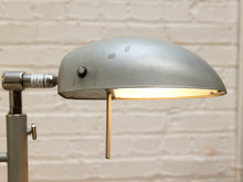 Load image into Gallery viewer, Close-up of the floor lamp's illuminated gray metal dome shade, showing the control knob and adjustable joint against a white brick wall.
