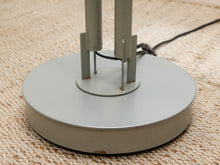 Load image into Gallery viewer, Close-up of the floor lamp's round silver-gray metal base and two vertical supports on a beige woven rug.
