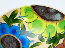 Load image into Gallery viewer, Close-up of a hand-painted ceramic plate featuring vibrant blue flowers, green leaves, and lime-green and dark brown abstract shapes on a cream background.
