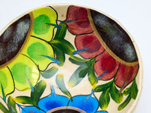 Load image into Gallery viewer, Close-up of a hand-painted ceramic bowl interior featuring a colorful floral pattern with green, red, blue, and dark brown motifs on a cream background.
