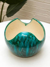 Load image into Gallery viewer, A ceramic bowl with a wavy, asymmetrical rim, featuring a glossy teal and green marbled exterior and a matte cream-colored interior, set on a white surface.
