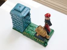 Load image into Gallery viewer, A vintage cast iron artillery bank featuring a blue powder horn, a soldier figurine with a red hat, and a gold cannon on a green base with 'ARTILLERY BANK' written in gold letters.
