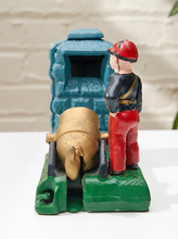 Load image into Gallery viewer, A vintage-style hand-painted toy or figurine depicting a soldier standing beside a large cannon mounted on a green base, with a blue structure behind it, displayed on a white surface against a light brick wall background.
