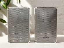 Load image into Gallery viewer, Pair of vintage silver-gray bookshelf stereo speakers with perforated metal front grilles, softly rounded rectangular cabinets, and attached speaker wires

