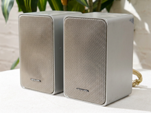 Load image into Gallery viewer, Pair of vintage silver-gray bookshelf stereo speakers with perforated metal front grilles, softly rounded rectangular cabinets, and attached speaker wires


