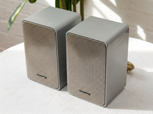 Load image into Gallery viewer, Pair of vintage silver-gray bookshelf stereo speakers with perforated metal front grilles, softly rounded rectangular cabinets, and attached speaker wires

