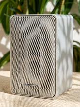 Load image into Gallery viewer, Pair of vintage silver-gray bookshelf stereo speakers with perforated metal front grilles, softly rounded rectangular cabinets, and attached speaker wires

