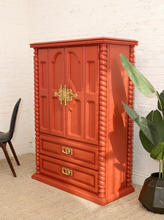 Load image into Gallery viewer, Vintage deep red painted armoire with double cabinet doors, ornate gold-tone handles, carved spiral side columns, raised decorative panels, and two lower drawers
