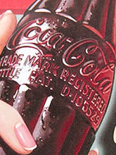 Load image into Gallery viewer, A close-up of a hand holding a vintage glass Coca-Cola bottle, showing the embossed Coca-Cola script and registration text on the bottle against a dark background.
